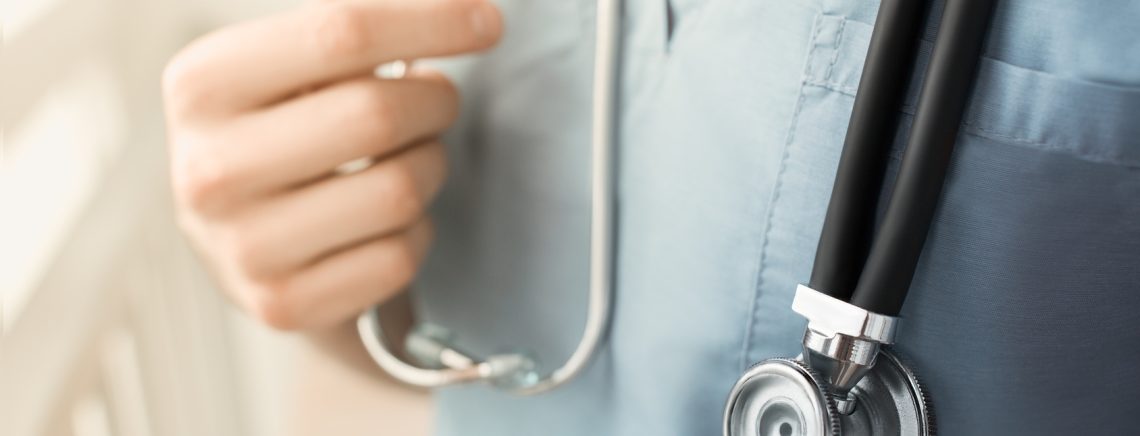 A young female doctor in a blue smock holding a phonendoscope in arms. Blurred background. Concept of medical help. Light effect.
