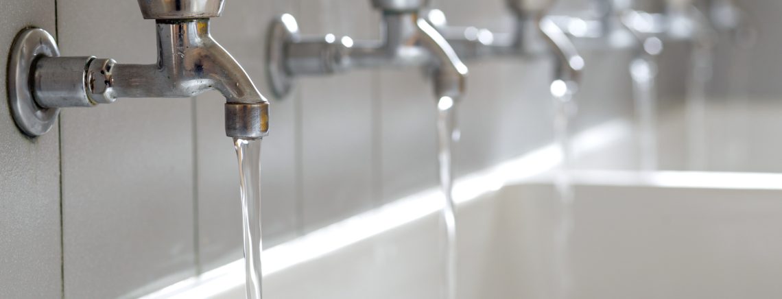 many steel taps with drinking water flowing in college bathroom
