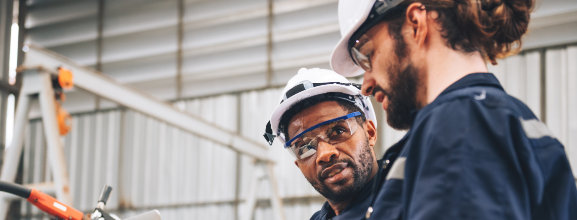 Two workers in safety gear discussing paperwork.